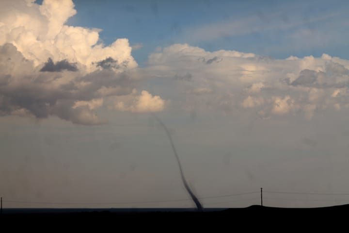 a thin landspout tornado rising into a blue and clouded sky