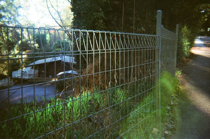 Hazy film photo through a wire fence showing a house in the background