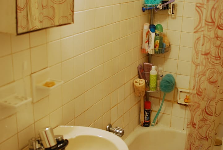 warm toned photo of a small bathroom showing a shower caddy and white tile