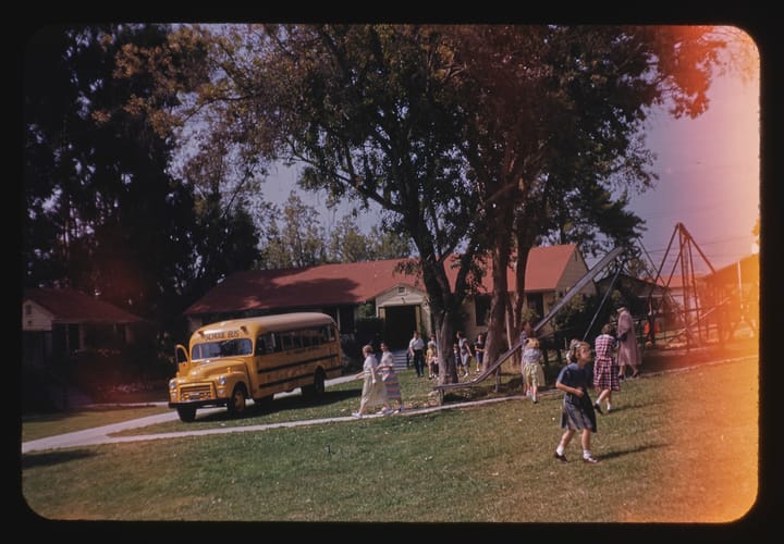 children and adults near a playground with a school bus in background